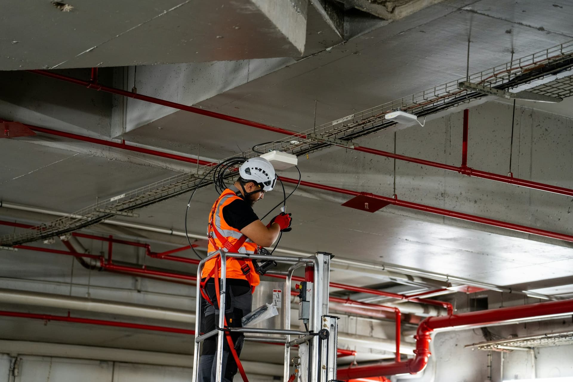 Technician on a lift installing overhead services among red fire-protection pipes