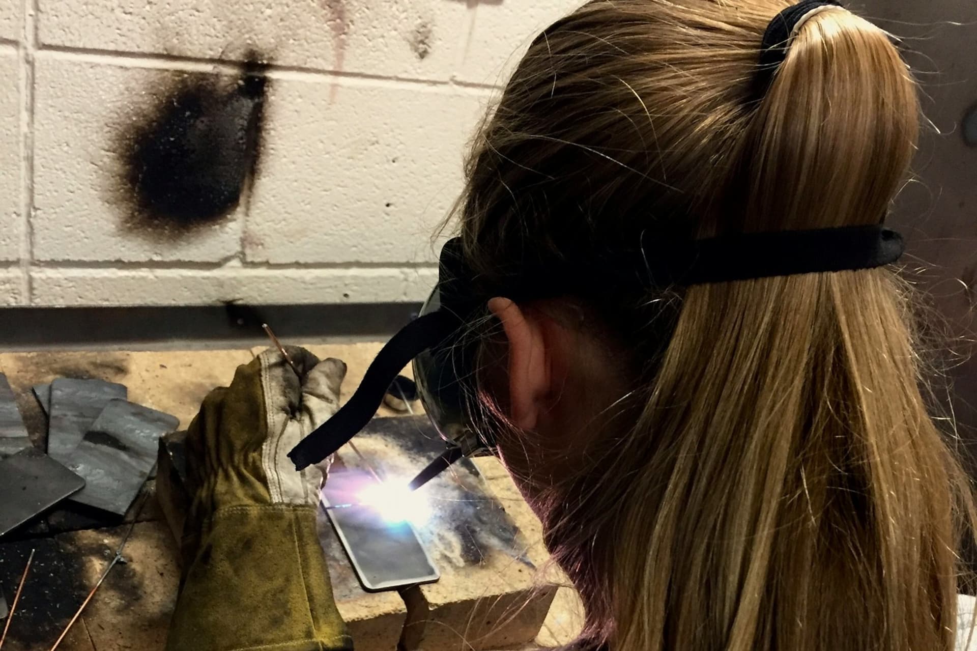 Welder in eye protection welding steel plate at a workbench